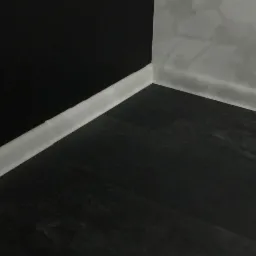 Ciemna podłoga z paneli, biała listwa przypodłogowa przy czarnej i szarej ścianie w rogu pokoju.