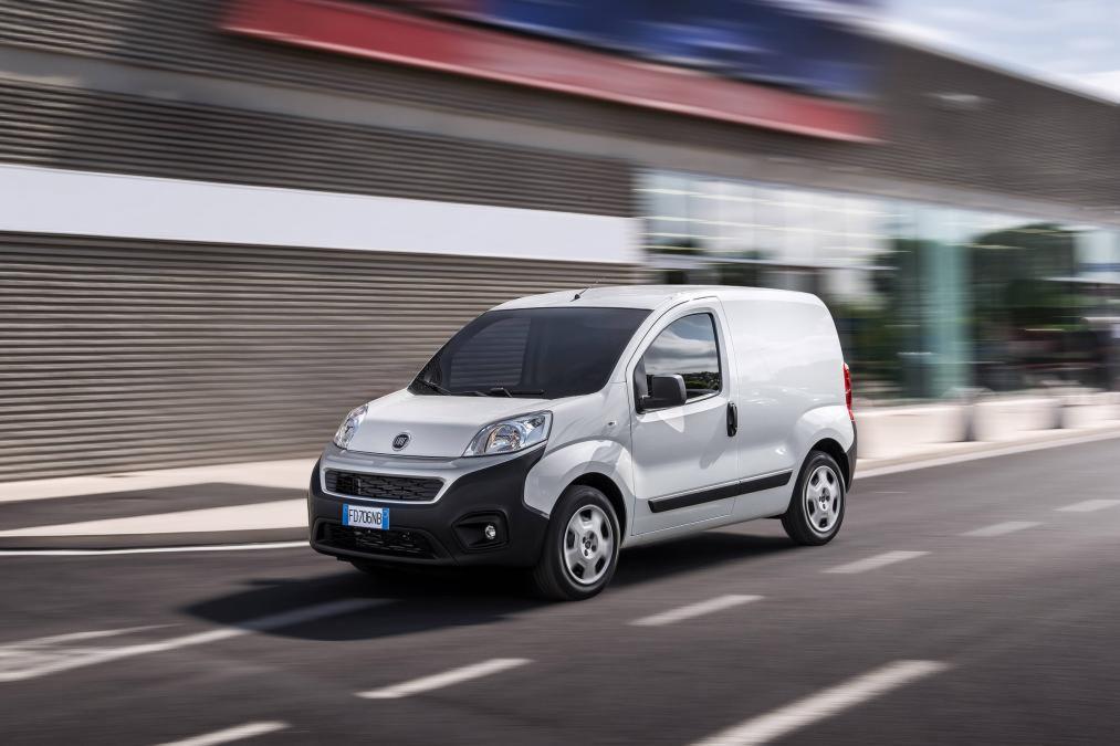 Biały samochód dostawczy Fiat Fiorino w ruchu, widziany z boku na tle nowoczesnego budynku w Krzeszowie.