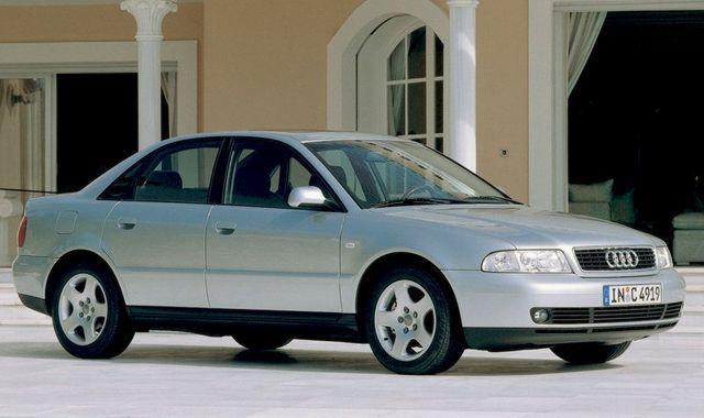 Srebrny sedan Audi A4 zaparkowany przed budynkiem z kolumnami, widok z boku, tablica rejestracyjna widoczna.