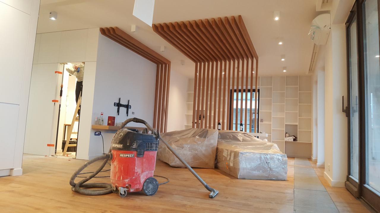 Wnętrze w trakcie wykańczania: widoczny pracownik na drabinie, odkurzacz przemysłowy marki Respect, drewniane lamele na suficie i ścianach, oraz meble zabezpieczone folią.