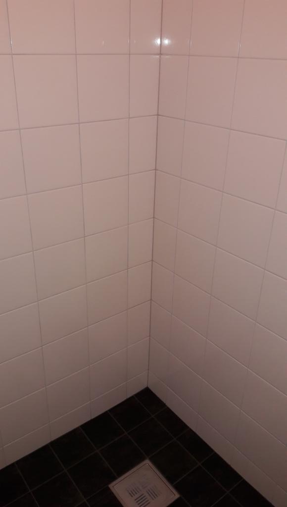 Narożnik wykafelkowanej kabiny prysznicowej z jasnymi płytkami ściennymi i ciemnymi płytkami podłogowymi, widoczny odpływ liniowy.