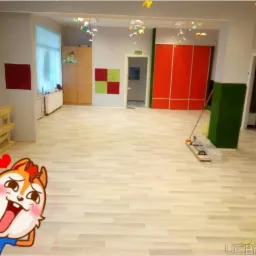 Wnętrze pokoju po remoncie z jasną podłogą, czerwonymi szafami w tle i dekoracjami na suficie, widoczne narzędzia do sprzątania i paleta. Na pierwszym planie naklejka.