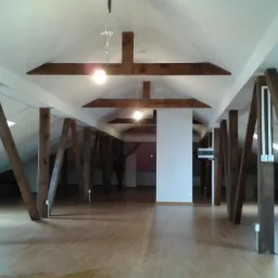 Przestronne, jasne poddasze po remoncie z drewnianymi belkami konstrukcyjnymi i nową podłogą, widoczne okna dachowe i oświetlenie.