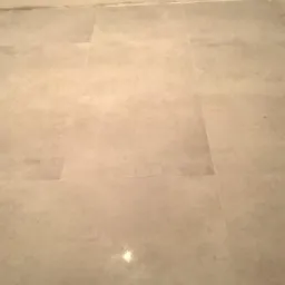 Ułożone szare płytki podłogowe w trakcie prac wykończeniowych, widoczny fragment ściany z gniazdkiem elektrycznym i zabezpieczona folią krawędź podłogi.