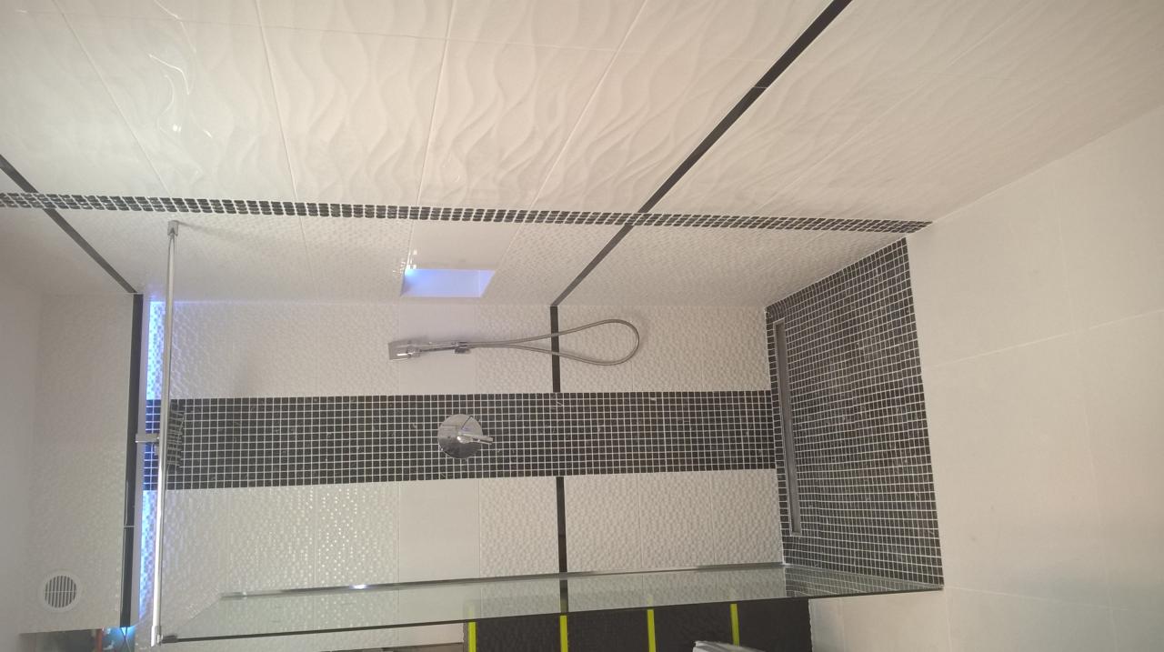 Wykończona łazienka z biało-czarnymi płytkami, kabiną prysznicową ze szklaną ścianką, chromowaną armaturą i podświetlanym sufitem.