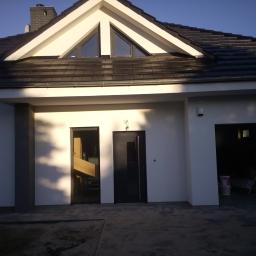 MPG Usługi ogólnobudowlane - Nowoczesny dom jednorodzinny z białymi ścianami, ciemną dachówką i antracytowymi oknami oraz drzwiami wejściowymi, widziany z zewnątrz w słoneczny dzień.