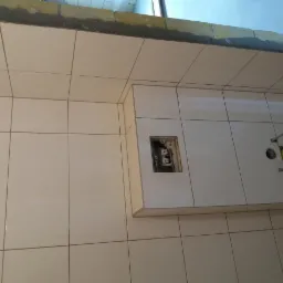 Ściana łazienki wyłożona jasnymi, błyszczącymi płytkami ceramicznymi z widocznymi otworami na instalacje sanitarne i elektryczne, w trakcie montażu.