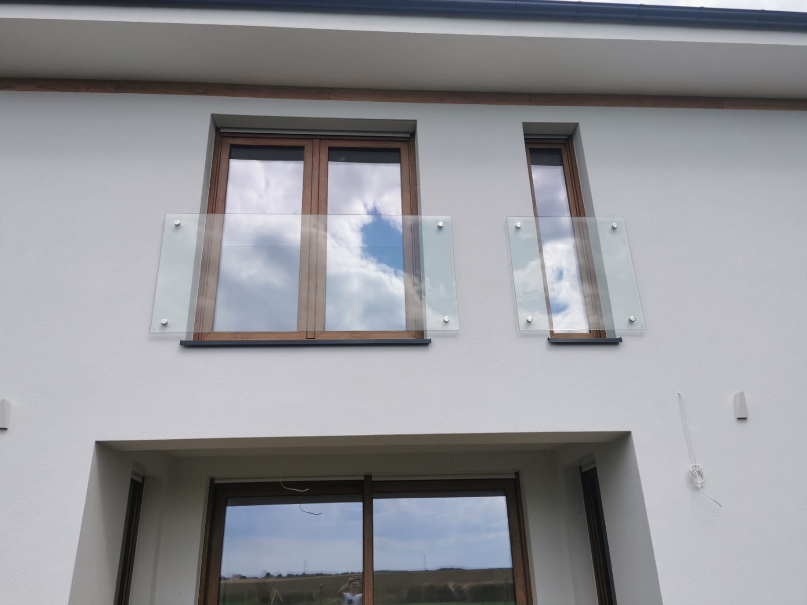 Elewacja budynku z oknami z drewnianą ramą i szklanymi balustradami mocowanymi na metalowe śruby.