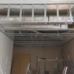 wykonczenia.waw.pl Andrzej Ostrowski - Metalowa konstrukcja sufitu podwieszanego z widocznymi przewodami i izolacją termiczną, w trakcie adaptacji lokalu, widoczny fragment ściany z płyt gipsowo-kartonowych.