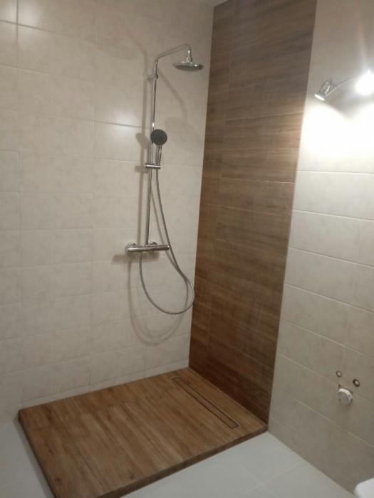 Nowoczesna kabina prysznicowa z drewnopodobną płytką na podłodze i ścianie, chromowana armatura, odpływ liniowy w podłodze.