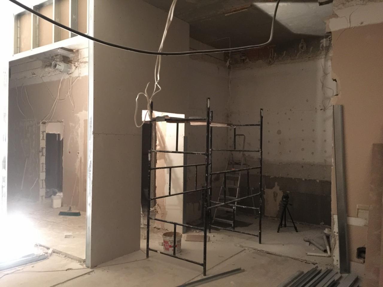 Wnętrze w trakcie prac adaptacyjnych pod żłobek: widoczne ściany w surowym stanie, konstrukcja rusztowania, przewody elektryczne zwisające z sufitu i częściowo położona gładź na ścianach.