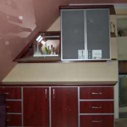 Zabudowa kuchenna w kolorze ciemnego drewna z aluminiowymi obramowaniami, szafka wisząca z mlecznymi szybami, półka z oświetleniem i butelkami, dopasowana do skosu dachu.