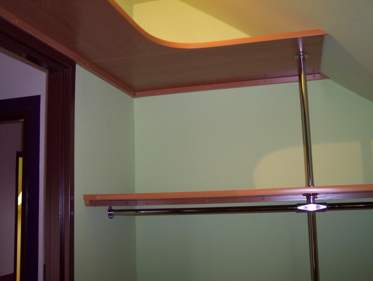 Półki z drewna i metalu w narożniku pomieszczenia z zielonymi ścianami, widoczny fragment rury chromowanej i drążka na ubrania.