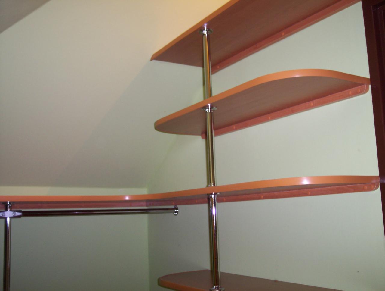 Półki z płyty wiórowej w kolorze jasnego drewna, zamocowane na metalowych rurach, dopasowane do skośnej ściany na poddaszu, widok z dołu.