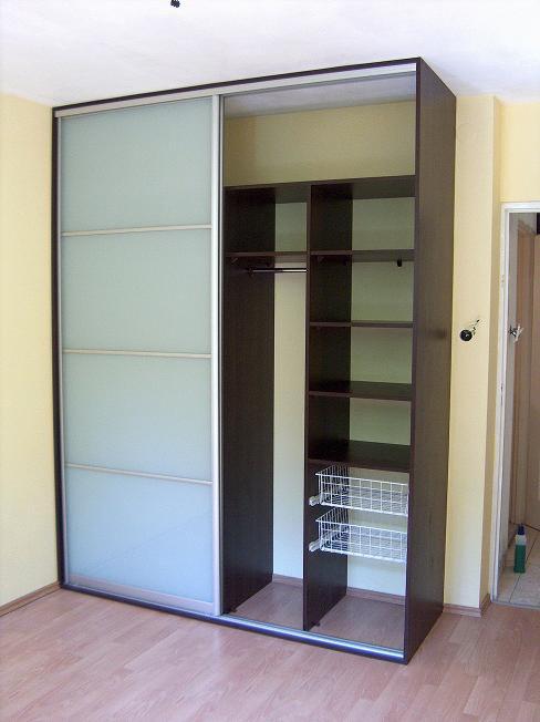 Ciemnobrązowa szafa wnękowa z przesuwnymi drzwiami z mlecznego szkła, widoczne wewnętrzne półki i wysuwane kosze druciane.