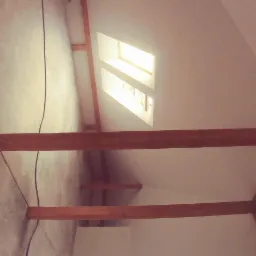 Poddasze z drewnianą konstrukcją nośną, surowy beton na podłodze i widoczne okno dachowe, przygotowane do dalszych prac wykończeniowych.