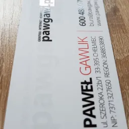 Wizytówka firmy PawGaw.pl z danymi kontaktowymi: imię i nazwisko, adres, numery telefonów, adres e-mail oraz adres strony internetowej. Wizytówka leży na drewnianej powierzchni.