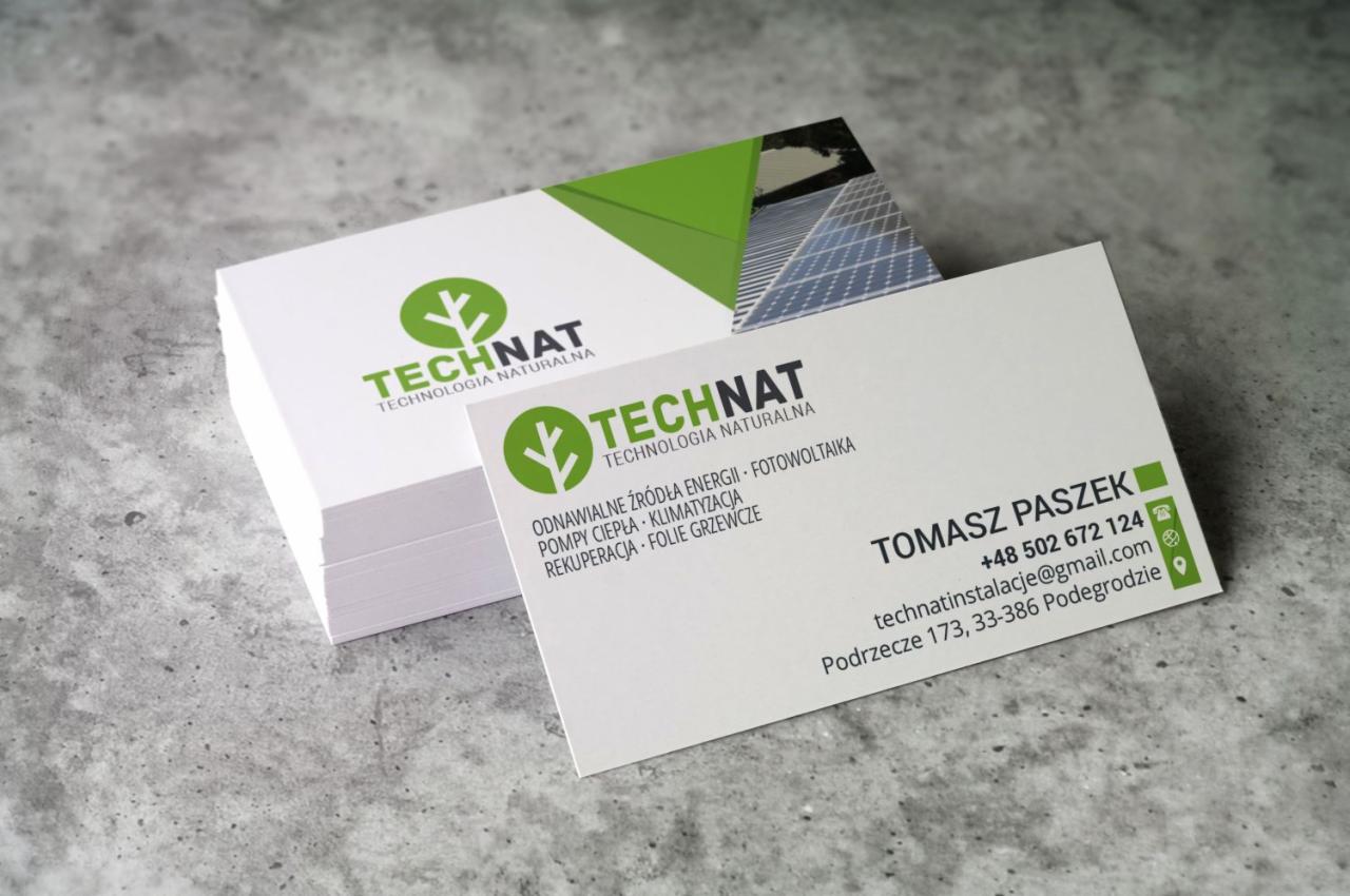 Stos wizytówek firmy Technat, z logo w kolorze zielonym przedstawiającym stylizowane drzewo i panele fotowoltaiczne w tle, na szarym, teksturowanym podłożu.