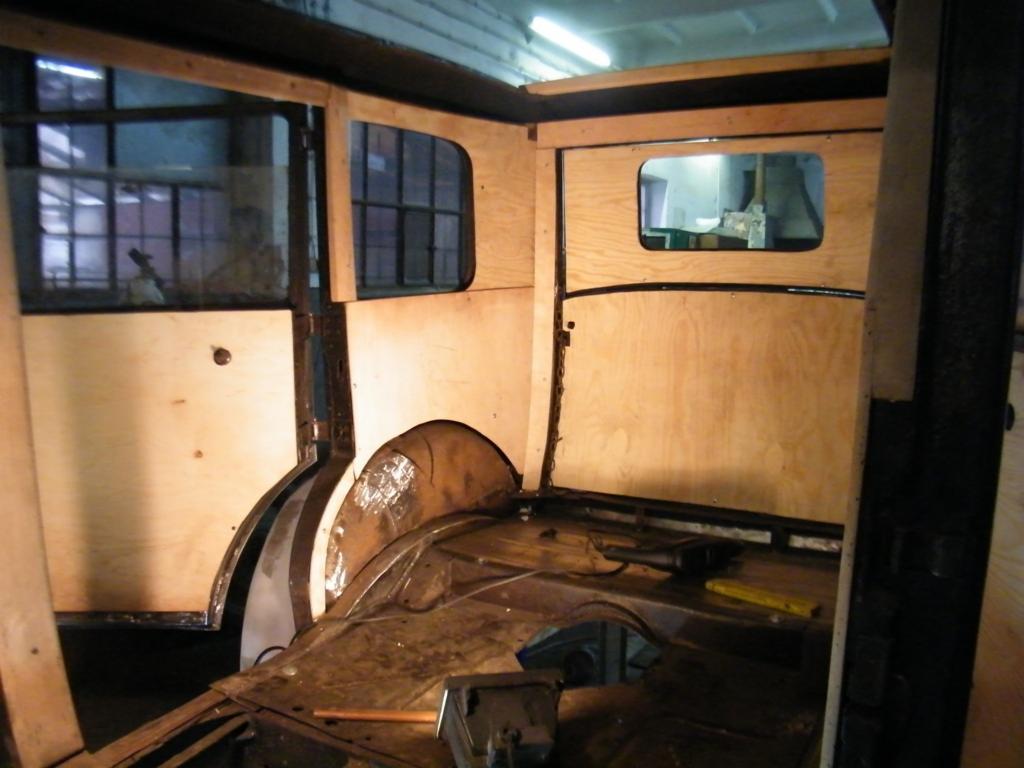 Wnętrze odrestaurowywanego klasycznego samochodu z drewnianymi panelami, widoczne elementy karoserii i okna, w trakcie prac renowacyjnych.