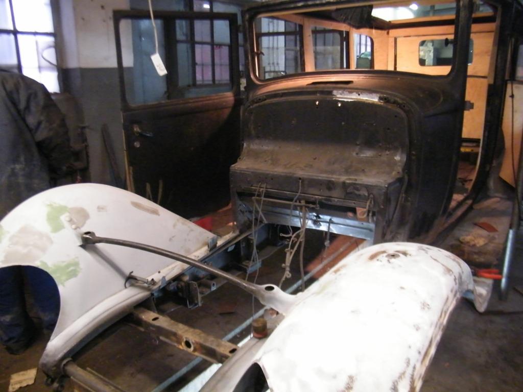 Fragment nadwozia starego samochodu w trakcie renowacji, z widocznymi elementami karoserii i ramą podwozia w warsztacie.