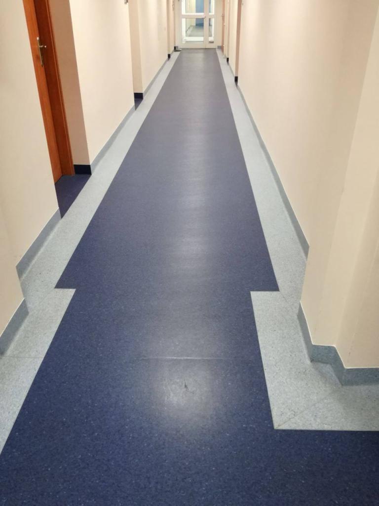 Długi korytarz z granatową wykładziną podłogową i jasnoszarymi listwami przypodłogowymi, widok z perspektywy.