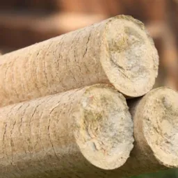 Trzy cylindryczne pale brykietu drzewnego trzymane w dłoni, ukazujące strukturę i teksturę materiału na tle rozmytej zieleni.