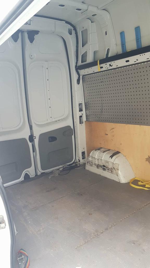 Wnętrze białego furgonetki z widoczną podłogą z fakturą, tylnymi drzwiami i ścianą działową z perforowanej blachy.