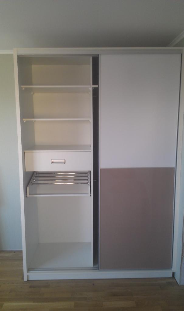 Biała szafa wnękowa z przesuwnymi drzwiami, z widocznymi półkami, szufladą i metalowym wieszakiem na spodnie.