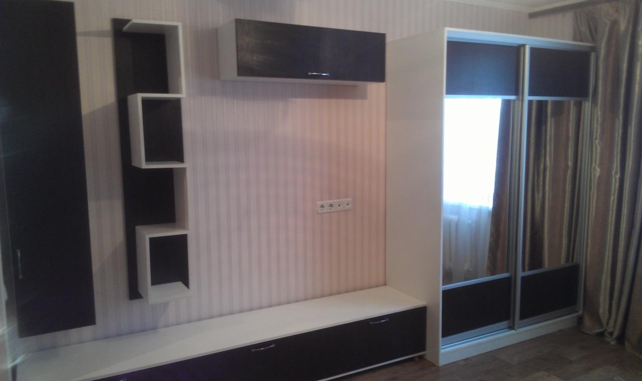 Zabudowa meblowa w salonie w Nowym Miasteczku: szafa przesuwna z lustrami, wisząca szafka, półki modułowe i szafka RTV w kolorach bieli i ciemnego brązu na tle ściany w pionowe pasy.