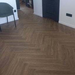 Tomek - Ułożona podłoga z paneli w jodełkę, widoczne fragmenty krzesła i drzwi w kolorze granatowym.