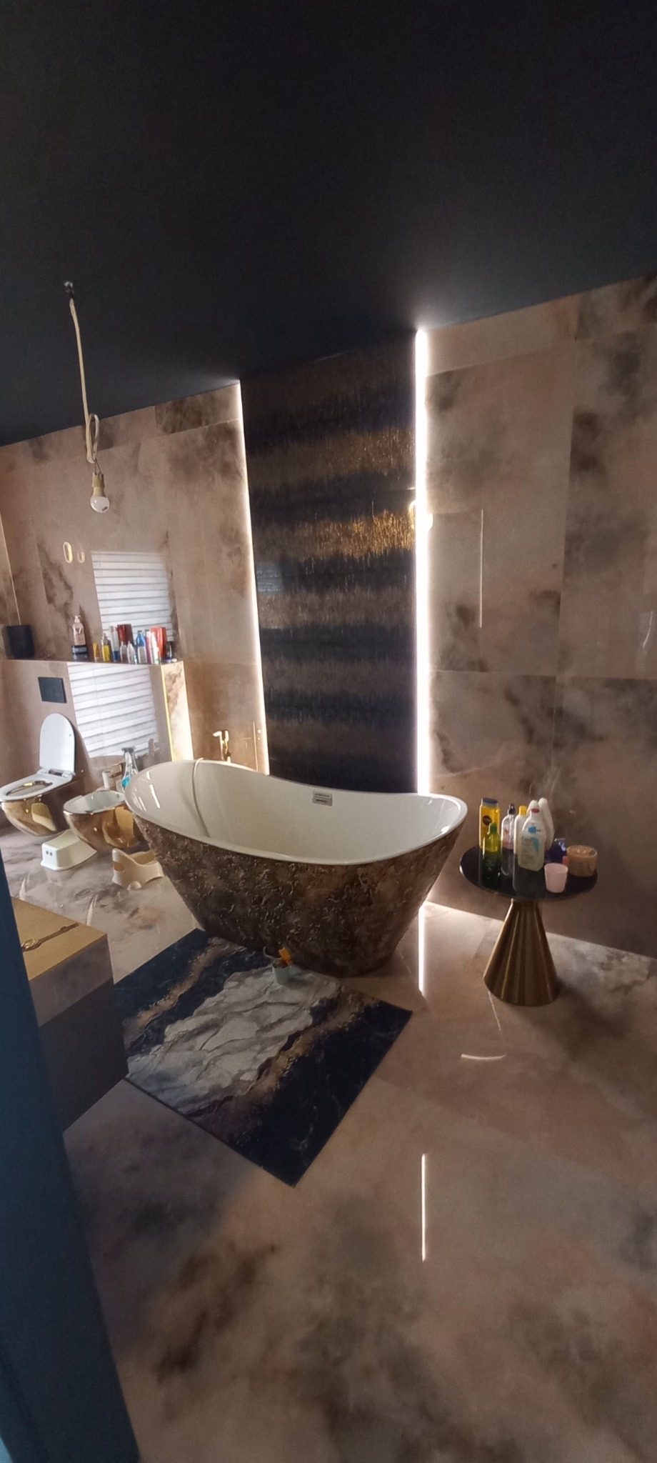 Luksusowa łazienka z wolnostojącą wanną o teksturze kamienia, pasującą do marmurowych płytek na ścianach i podłodze, oświetlona pionowymi pasami światła LED.