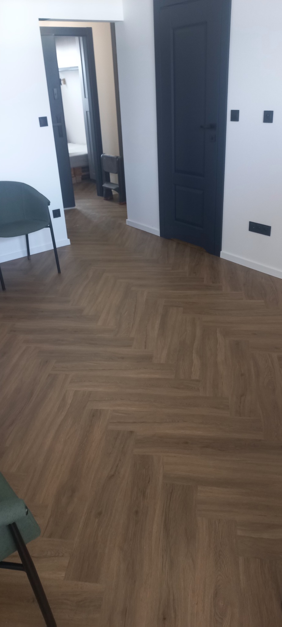 Ułożona podłoga z paneli w jodełkę, widoczne fragmenty krzesła i drzwi w kolorze granatowym.