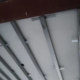 Montaż stelaża sufitu podwieszanego z płyt kartonowo-gipsowych, widoczne profile stalowe i elementy mocujące do stropu.