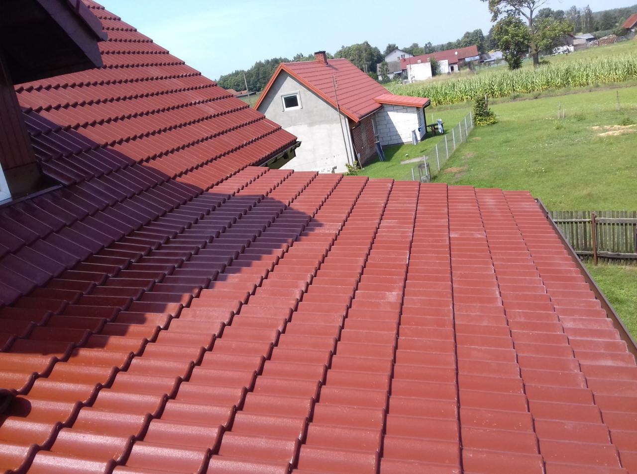 Nowy dach z czerwonej dachówki ceramicznej, widok z góry, w tle domy i pole kukurydzy.