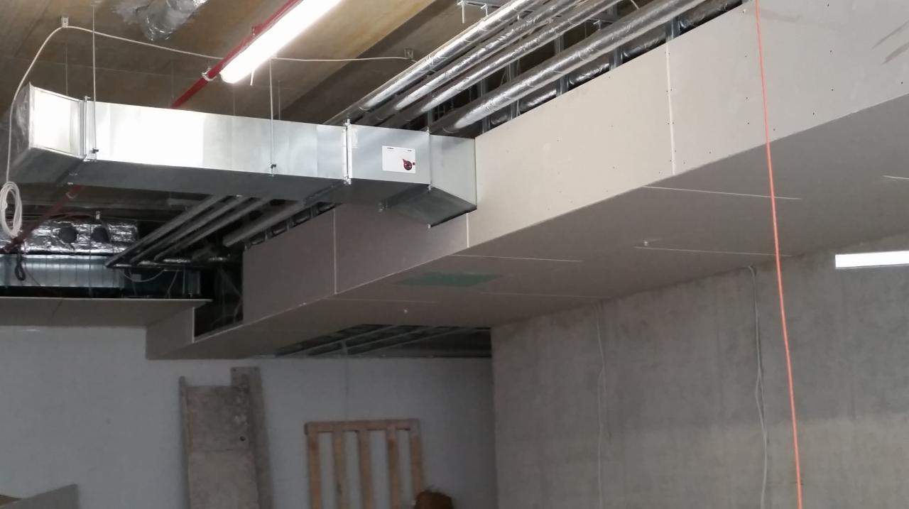 Montaż instalacji wentylacyjnej pod sufitem z płyt gipsowo-kartonowych, widoczne rury wentylacyjne i element oświetlenia liniowego.