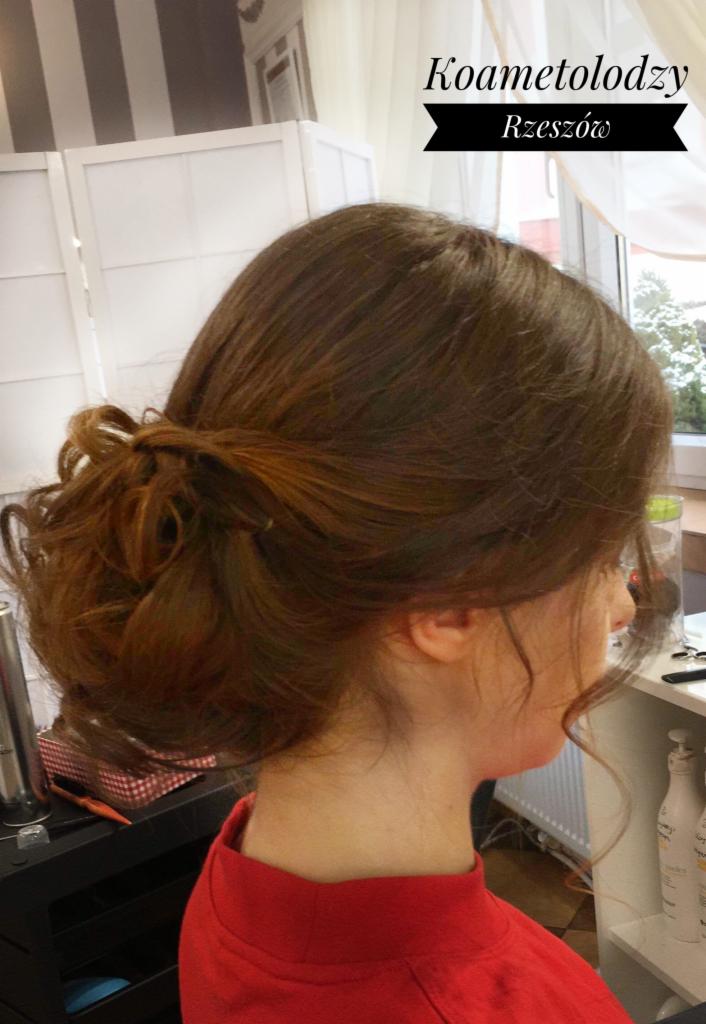 Upięcie włosów w stylu messy bun, brązowe włosy z delikatnymi refleksami, widok z profilu, w tle widać okno i regał z kosmetykami.