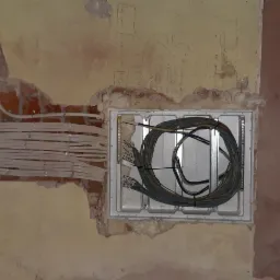 Wiązka białych kabli elektrycznych ułożonych w bruzdach w ceglanej ścianie, obok puszki instalacyjnej z nawiniętymi kablami, na tle surowych ścian w trakcie remontu.