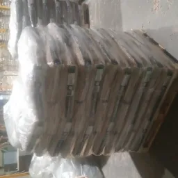 Ułożone na palecie, owinięte folią pakiety pelletu drzewnego w magazynie, widoczne inne palety w tle.