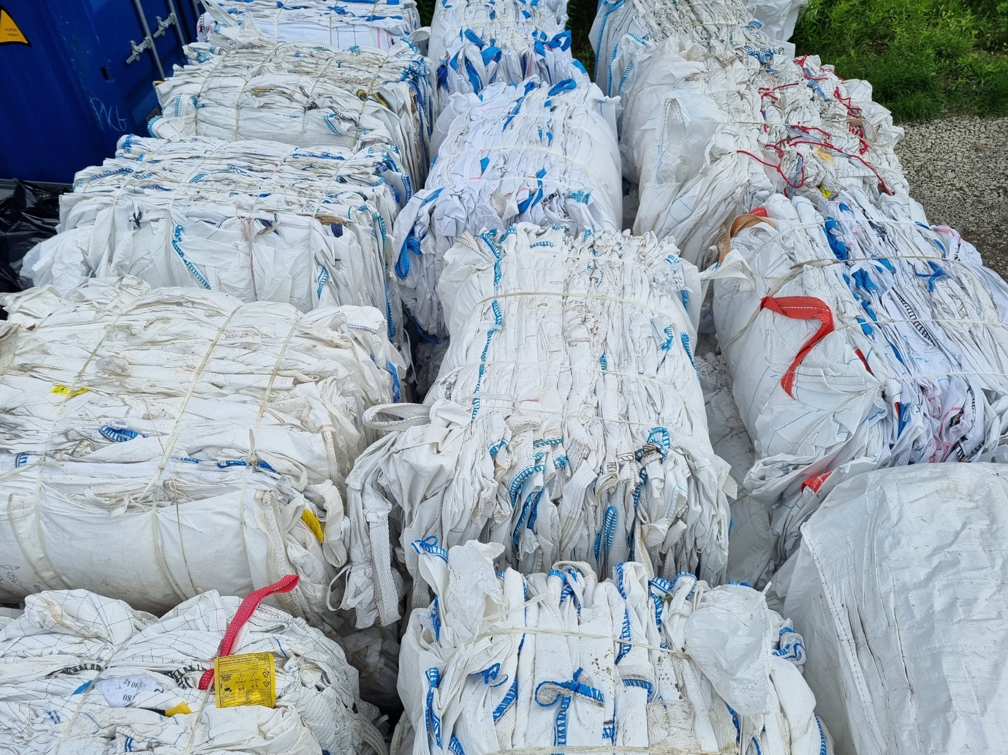 Stosy sprasowanych, białych worków big bag z niebieskimi i czerwonymi elementami, zabezpieczonych sznurkiem, składowane w Mielcu, prawdopodobnie do recyklingu.