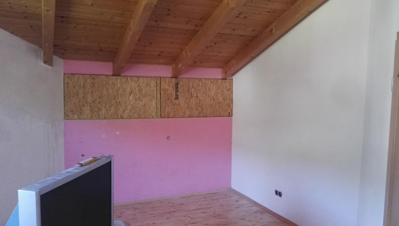 Poddasze w trakcie adaptacji: ściana z różową izolacją, płyty OSB pod drewnianym stropem, widoczne gniazdka elektryczne na białej ścianie.