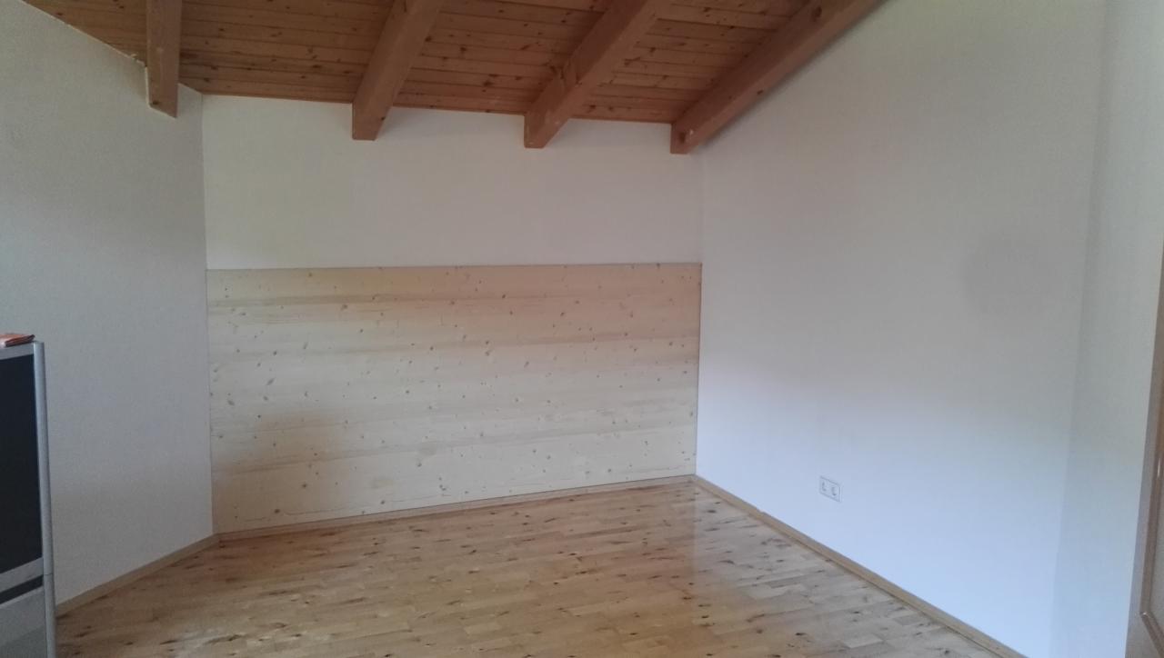 Pokój na poddaszu z drewnianym sufitem i częściowo wykończoną ścianą panelami z jasnego drewna, podłoga drewniana, białe ściany.