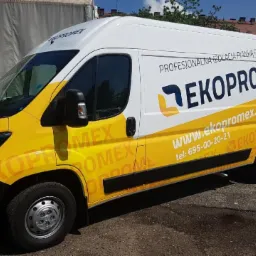 Żółto-biały samochód dostawczy firmy Ekopromex z reklamą izolacji pianką PUR, zaparkowany na zewnątrz z widocznymi budynkami w tle.