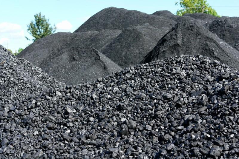 Góra węgla kamiennego, drobny i gruby sort, widoczne hałdy na tle błękitnego nieba i zieleni drzew.