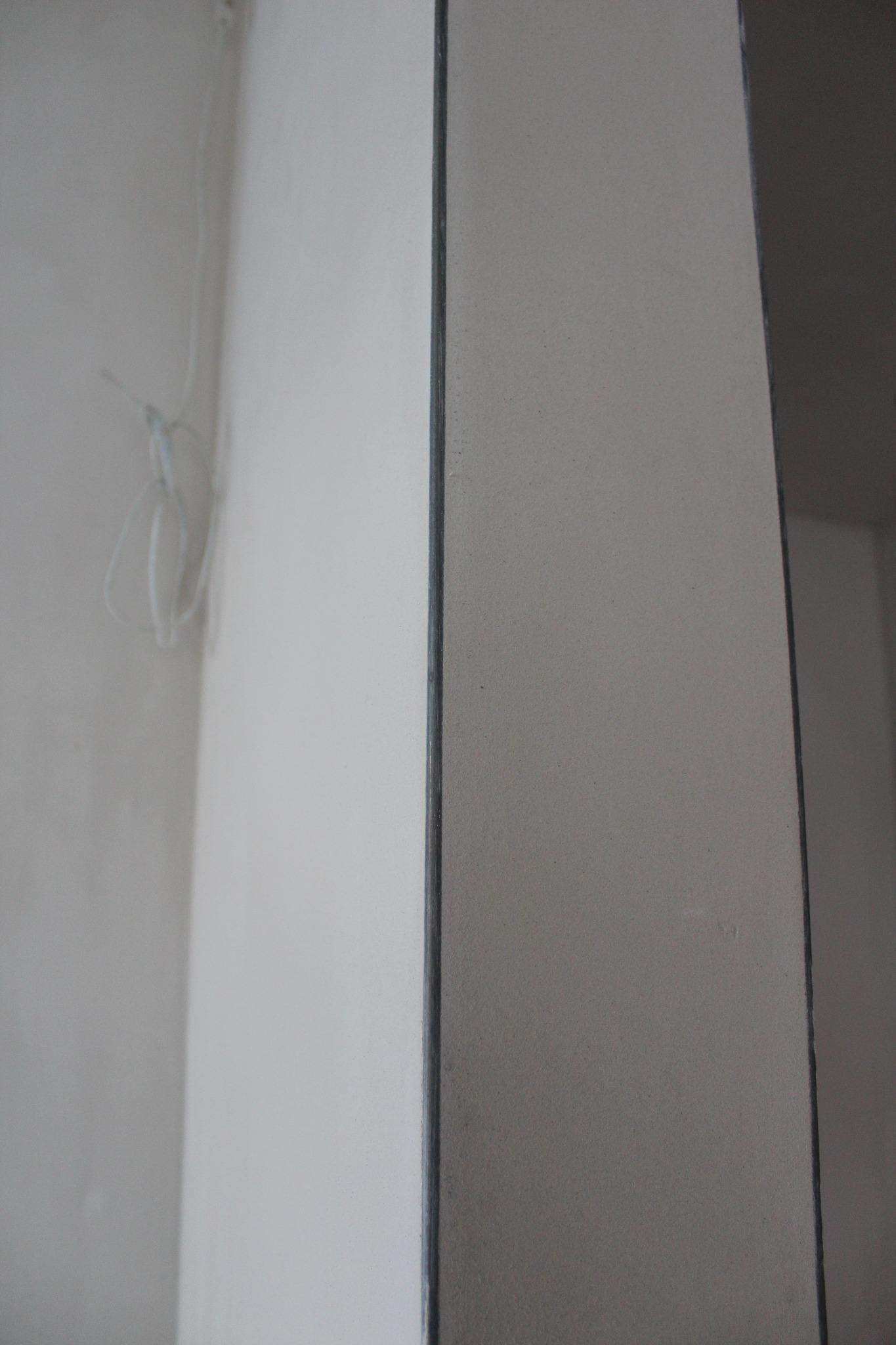 Gładka, jasna ściana po nałożeniu tynku, widoczne przewody elektryczne w rogu pomieszczenia.