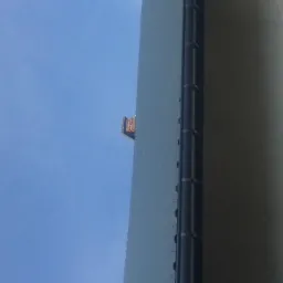 Nietypowy widok z dołu na ścianę budynku z rynną, fragment dachu widoczny na tle błękitnego nieba.