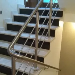 Nowoczesna, polerowana metalowa balustrada schodowa z poziomymi prętami, zamontowana na marmurowych stopniach z czarnymi podstopnicami, widok z dołu schodów.