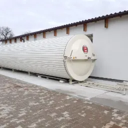 Długa, cylindryczna suszarnia do drewna marki Eberl, umieszczona na metalowej konstrukcji przed białą halą z brązowym dachem.