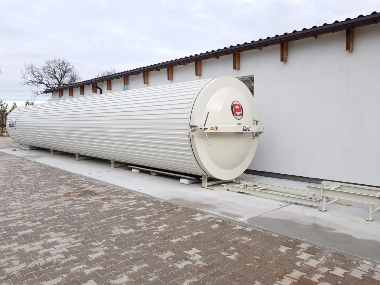Długa, cylindryczna suszarnia do drewna marki Eberl, umieszczona na metalowej konstrukcji przed białą halą z brązowym dachem.