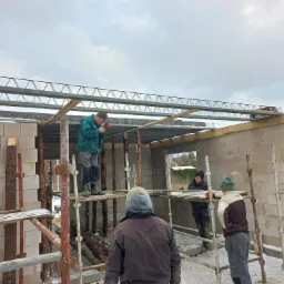 Budowa domu z bloczków: murarz na rusztowaniu montuje strop Teriva, widoczne zbrojenia i pustaki stropowe, zimowa sceneria.