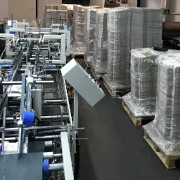 Automatyczna linia introligatorska w Chełmku, z widocznymi stosami gotowych, zapakowanych produktów na paletach w tle.